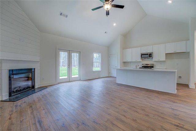 unfurnished living room with light wood finished floors, visible vents, a ceiling fan, a glass covered fireplace, and high vaulted ceiling