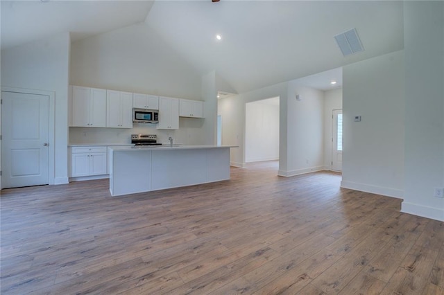 kitchen featuring a kitchen island with sink, white cabinetry, open floor plan, appliances with stainless steel finishes, and light wood-type flooring