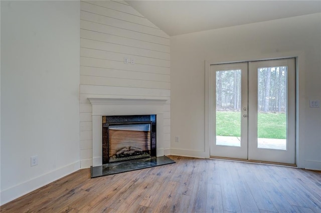 unfurnished living room featuring a fireplace with raised hearth, vaulted ceiling, wood finished floors, and french doors