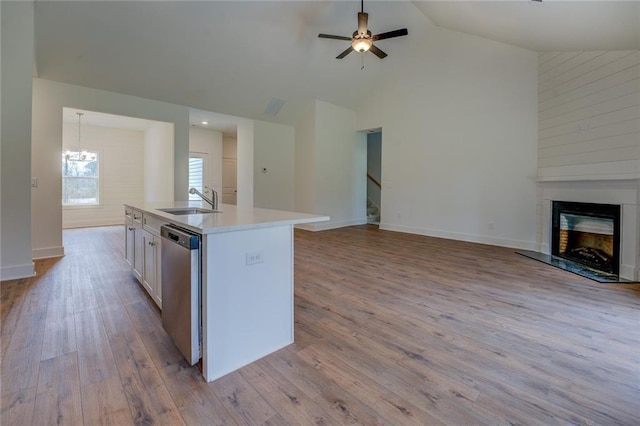 kitchen with a fireplace with raised hearth, open floor plan, wood finished floors, stainless steel dishwasher, and a sink