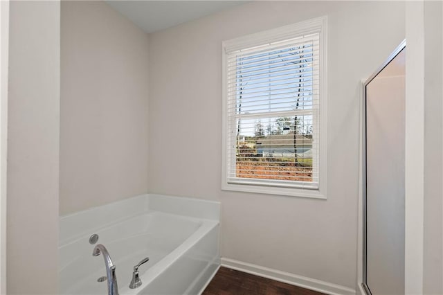 bathroom with a tub to relax in, plenty of natural light, and hardwood / wood-style flooring