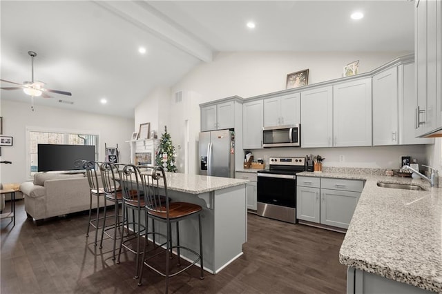 kitchen with dark wood-type flooring, sink, a kitchen island, light stone counters, and stainless steel appliances