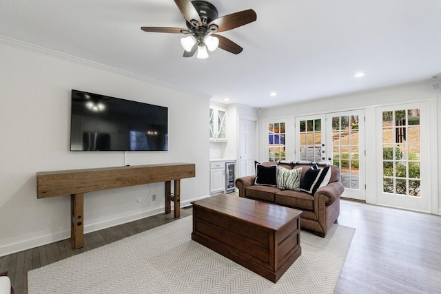 living room featuring beverage cooler, french doors, ceiling fan, light hardwood / wood-style flooring, and crown molding