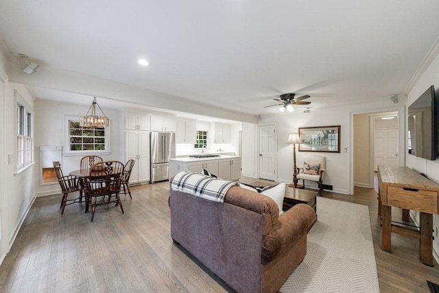 living room featuring ceiling fan with notable chandelier, sink, crown molding, and light hardwood / wood-style floors