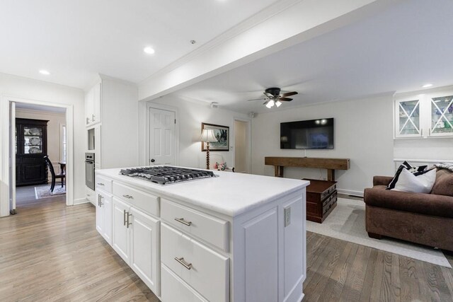 kitchen with appliances with stainless steel finishes, a center island, white cabinetry, light wood-type flooring, and ceiling fan