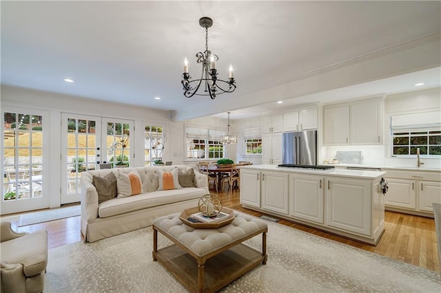 living room with sink, a chandelier, french doors, and light wood-type flooring