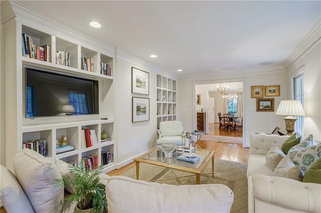 living room with light wood-type flooring, built in features, ornamental molding, and a notable chandelier