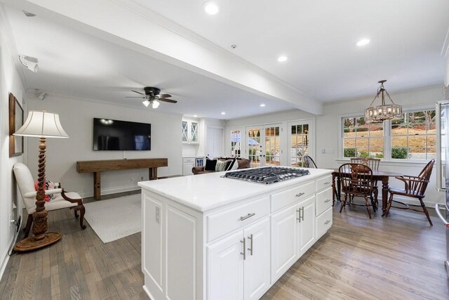 kitchen featuring a kitchen island, a wealth of natural light, white cabinetry, stainless steel gas cooktop, and ceiling fan with notable chandelier