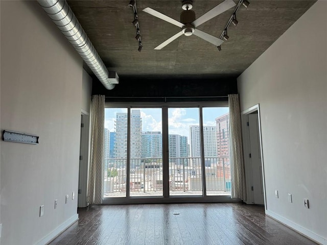 empty room featuring ceiling fan, plenty of natural light, rail lighting, and hardwood / wood-style floors