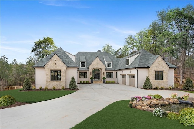 french country home with an attached garage, fence, driveway, stone siding, and a front yard