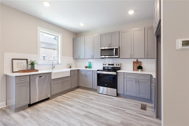 kitchen with light countertops, appliances with stainless steel finishes, a sink, and gray cabinetry