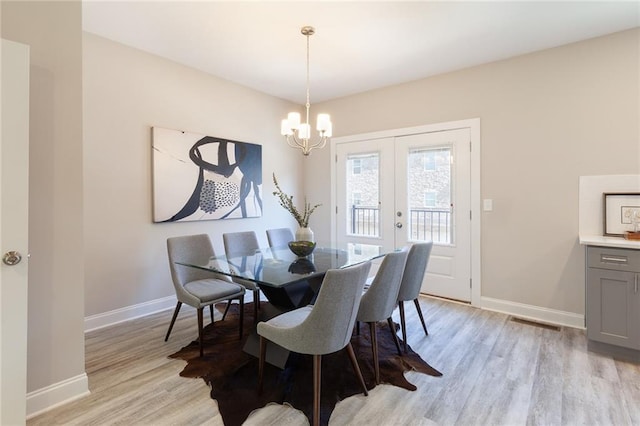 dining room with a chandelier, light wood-type flooring, visible vents, and baseboards