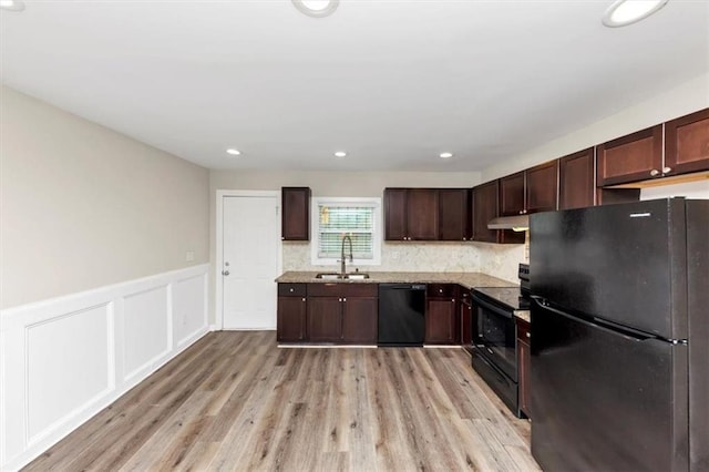 kitchen featuring light wood finished floors, dark brown cabinets, under cabinet range hood, black appliances, and a sink