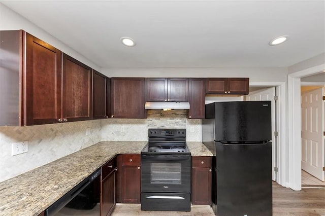 kitchen featuring light stone countertops, decorative backsplash, black appliances, under cabinet range hood, and light wood-type flooring