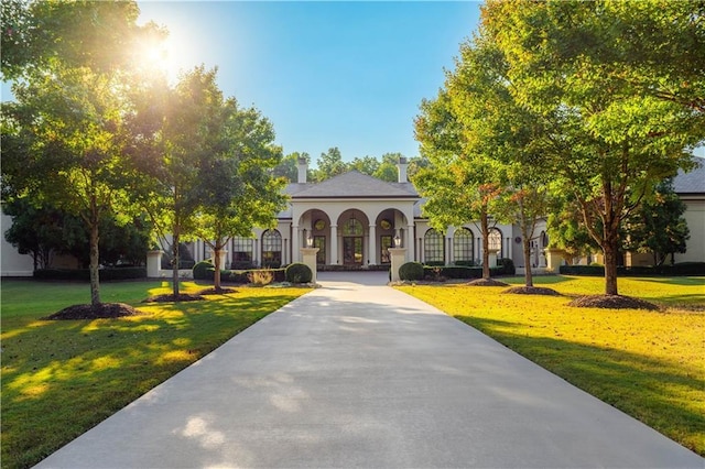 mediterranean / spanish-style house with stucco siding, a chimney, and a front lawn