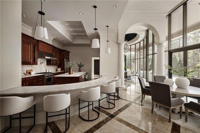 kitchen with high end range, ornamental molding, under cabinet range hood, ornate columns, and decorative backsplash