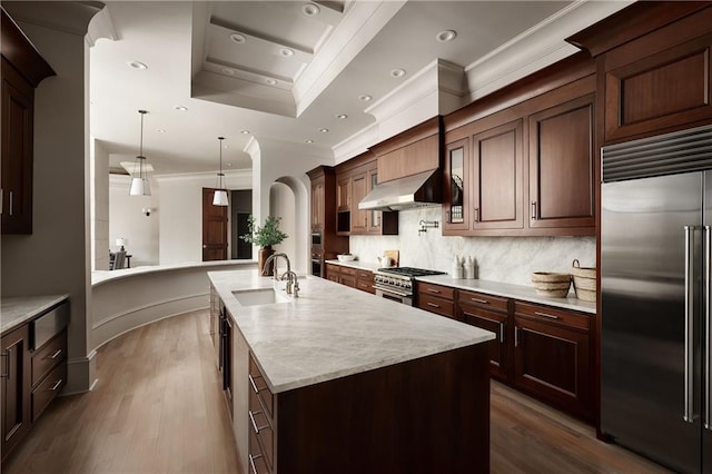 kitchen featuring premium appliances, a sink, a center island with sink, backsplash, and extractor fan