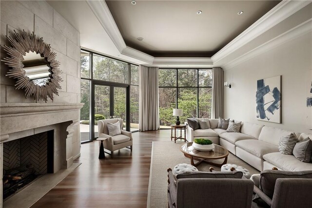 living room featuring a towering ceiling, ornamental molding, dark wood-style floors, a raised ceiling, and a premium fireplace