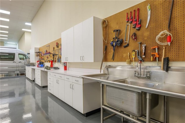 kitchen with a sink, white cabinetry, finished concrete flooring, and stainless steel countertops