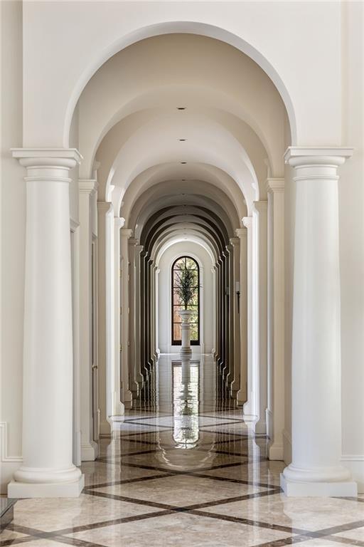 hall featuring arched walkways, baseboards, and marble finish floor