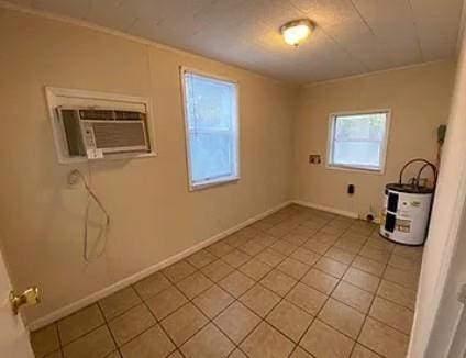 spare room with a wall mounted air conditioner, water heater, baseboards, and light tile patterned floors