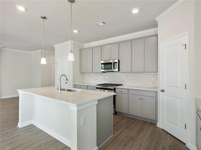 kitchen with gray cabinetry, sink, hanging light fixtures, stainless steel appliances, and a kitchen island with sink