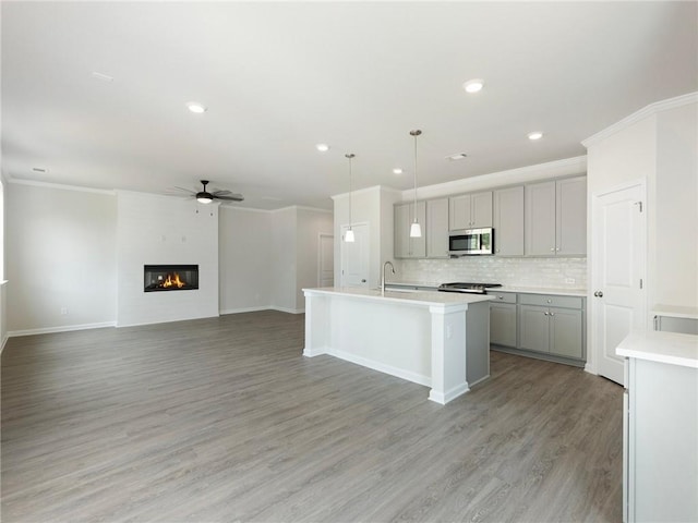 kitchen featuring backsplash, pendant lighting, gray cabinets, a fireplace, and a center island with sink