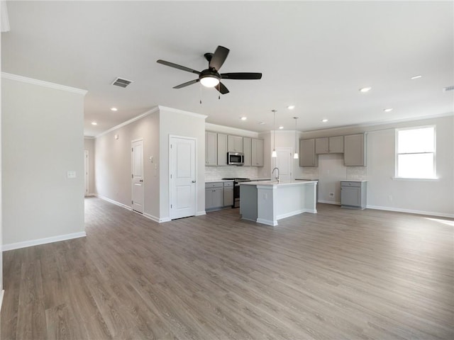 kitchen featuring gray cabinetry, decorative light fixtures, an island with sink, and appliances with stainless steel finishes