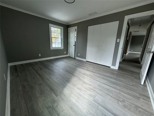 unfurnished bedroom with wood finished floors, baseboards, attic access, and ornamental molding