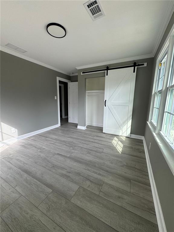 unfurnished bedroom featuring crown molding, baseboards, a barn door, wood finished floors, and a closet