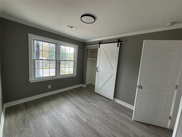 unfurnished bedroom featuring a barn door, wood finished floors, crown molding, and baseboards