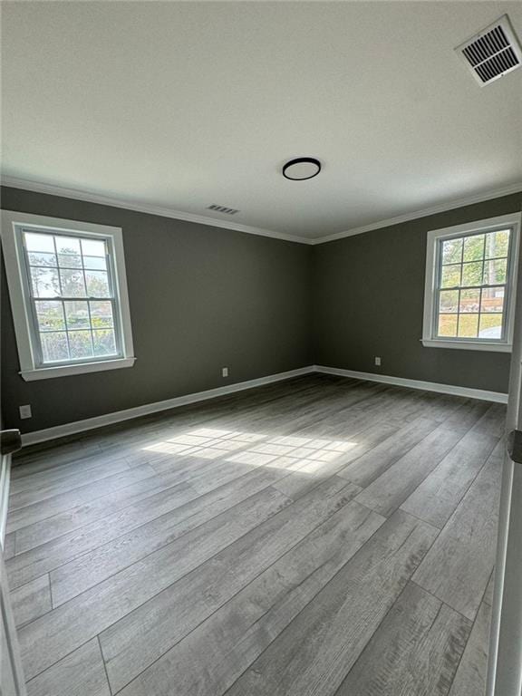 empty room featuring crown molding, baseboards, and wood finished floors