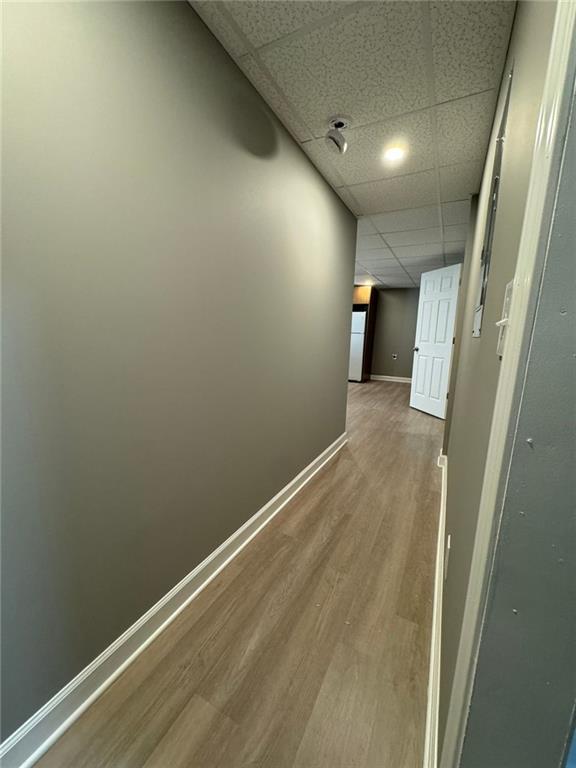 hallway featuring a drop ceiling, wood finished floors, and baseboards