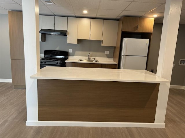 kitchen with freestanding refrigerator, black gas range oven, a sink, baseboards, and a paneled ceiling