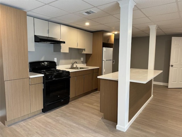 kitchen featuring black range with gas stovetop, under cabinet range hood, freestanding refrigerator, light wood finished floors, and a sink