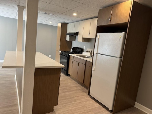 kitchen with freestanding refrigerator, black range with gas cooktop, light wood-style floors, light countertops, and a sink