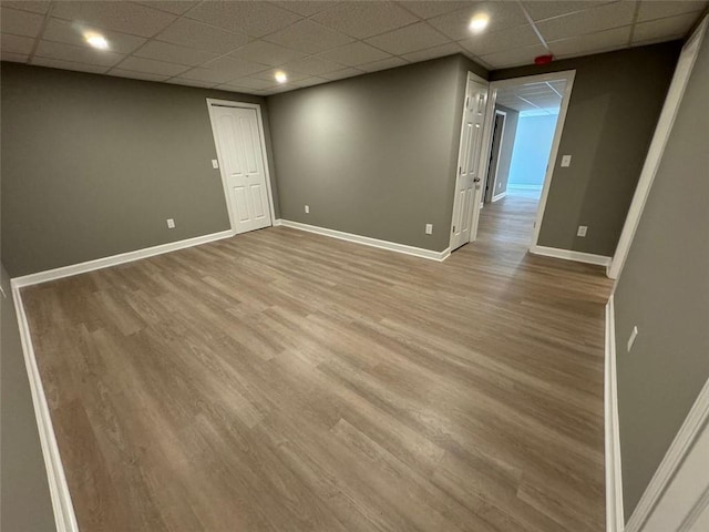 empty room featuring wood finished floors, baseboards, and a paneled ceiling