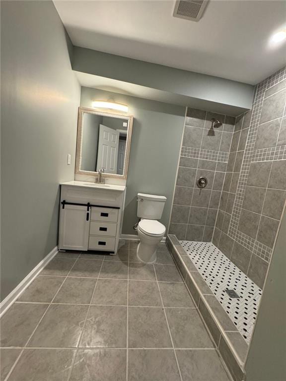bathroom featuring tile patterned floors, tiled shower, toilet, baseboards, and vanity