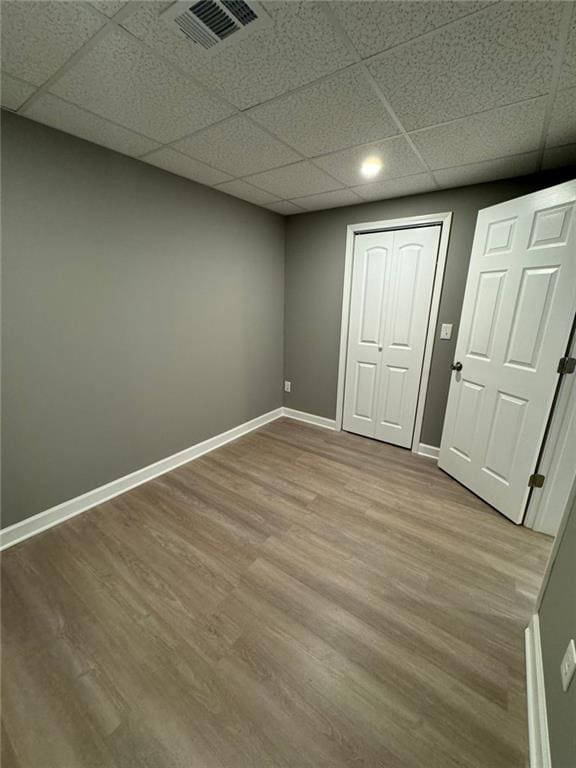 unfurnished bedroom featuring a drop ceiling, wood finished floors, baseboards, and a closet