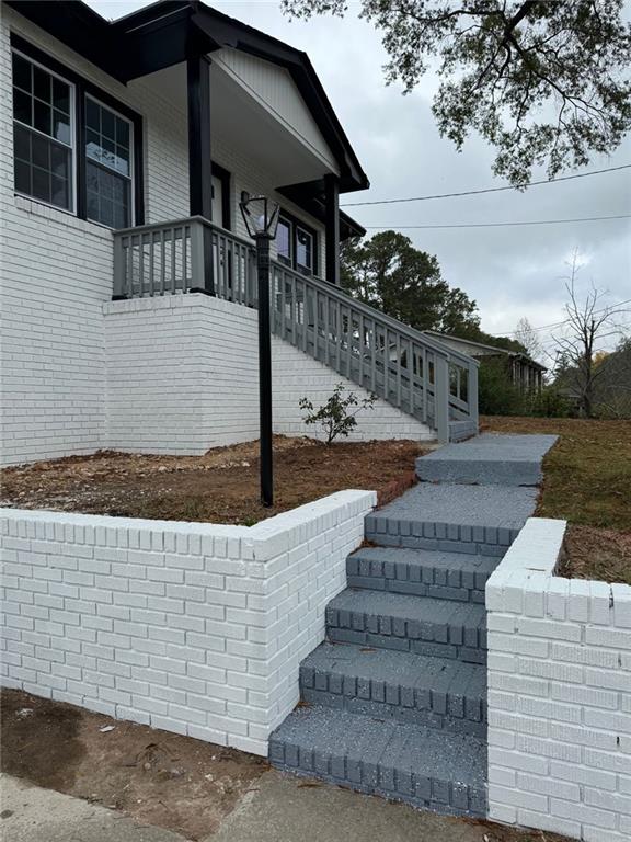 view of home's exterior with covered porch, stairs, and brick siding