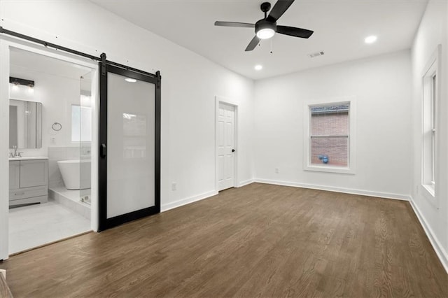 unfurnished bedroom with visible vents, a sink, a barn door, and dark wood-style flooring