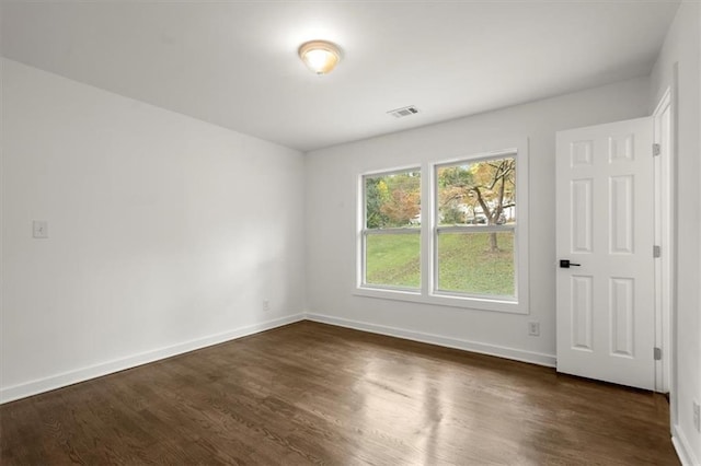 empty room featuring visible vents, baseboards, and dark wood finished floors