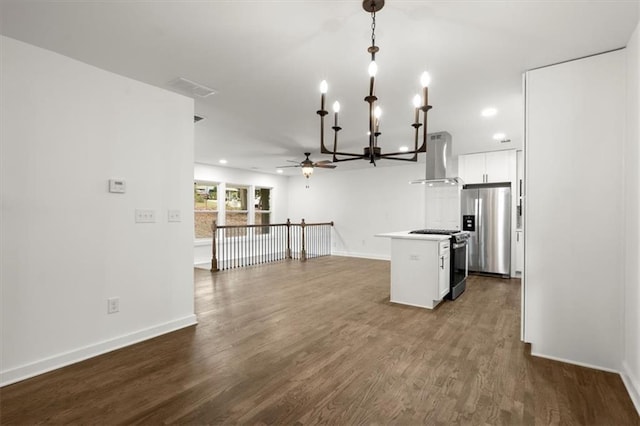 kitchen featuring dark wood-type flooring, wall chimney range hood, decorative light fixtures, white cabinets, and stainless steel appliances