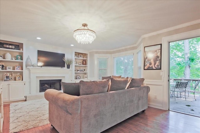 living area featuring built in features, wood finished floors, a fireplace, crown molding, and a notable chandelier