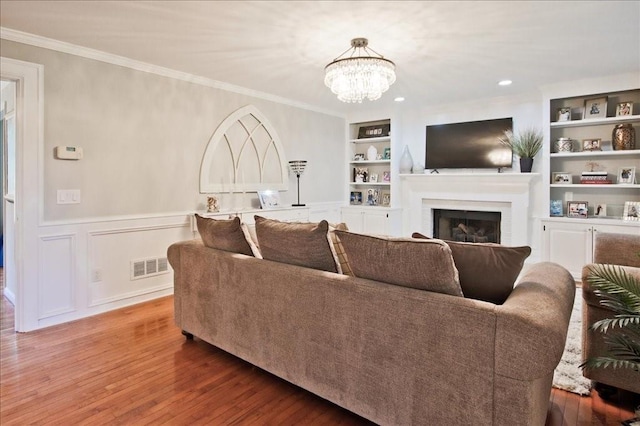 living room featuring visible vents, built in shelves, crown molding, a fireplace, and wood finished floors