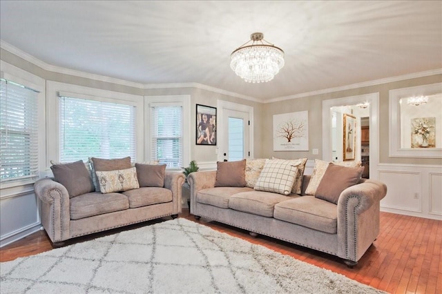 living area with wood-type flooring, a notable chandelier, ornamental molding, and a decorative wall