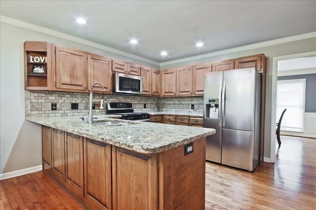 kitchen featuring appliances with stainless steel finishes, light wood-style floors, a peninsula, and a sink