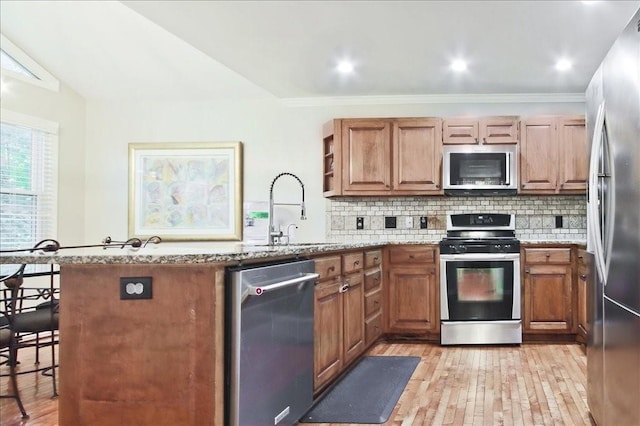 kitchen featuring decorative backsplash, a peninsula, light stone countertops, and stainless steel appliances