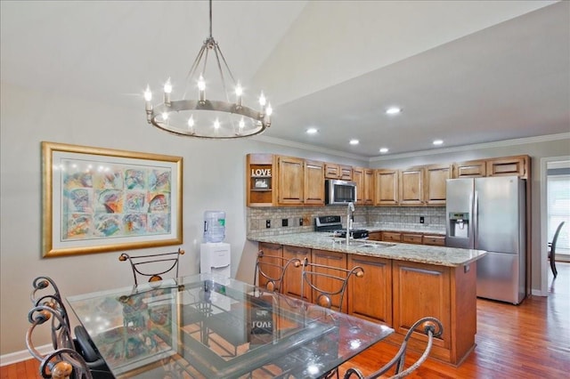 kitchen with wood finished floors, brown cabinetry, a peninsula, decorative backsplash, and appliances with stainless steel finishes