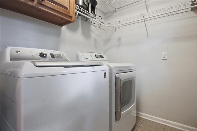 laundry room featuring washer and dryer, light tile patterned floors, cabinet space, and baseboards